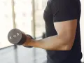 Mężczyzna w czarnej koszulce wykonuje ćwiczenia na biceps z hantlem 10 kg. To jedne z najlepszych ćwiczeń na biceps.
