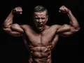 Mężczyzna z wyrzeźbionymi mięśniami napina bicepsy, krzycząc z wysiłku. Jego sylwetka sugeruje intensywny trening, być może z użyciem clenbuterolu.