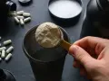 Łyżka białego proszku, czyli protein, trafia do shakera. Obok leżą kapsułki.