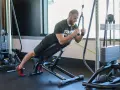 Mężczyzna wykonuje ćwiczenie na triceps, znane jako skull crushers, na ławce skośnej z użyciem wyciągu.