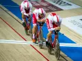 Trzech kolarzy w biało-czerwonych strojach ściga się na welodromie. Ich rowery i stroje mają logo ORLEN. To dynamiczne keirin kolarstwo.