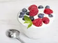 Pyszny jogurt z malinami i borówkami, idealny na śniadanie lub jako element diety jogurtowej. Obok leży łyżeczka.