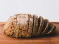 Pokrojony bochenek chleba żytniego na drewnianej desce. Zastanawiasz się, ile kcal ma kromka chleba?
