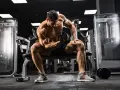 Mężczyzna z wyrzeźbionymi mięśniami wykonuje ćwiczenie na biceps z hantlem, skupiony na swoim **full body workout** w siłowni.