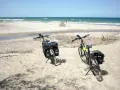 Dwa rowery z sakwami na piaszczystej plaży, gotowe do odkrywania tras rowerowych nad morzem.