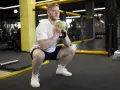Mężczyzna w białej koszulce wykonuje przysiad z zielonym kettlebell, który przypomina kształtem puchar.