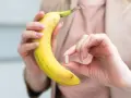 Kobieta trzyma banana i tabletkę, zastanawiając się, ile potasu dziennie powinna przyjmować.