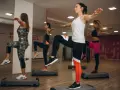 Kobiety ćwiczą aerobik na stepach, podnosząc kolana i wyciągając ręce.