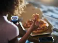 Kobieta trzyma kawałek pizzy i napój, czując głód. Grelina działa, apetyt rośnie.