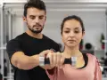 Trening dla początkujących: mężczyzna pomaga kobiecie podnosić hantle.
