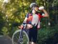 Kolarz w kasku i stroju sportowym pije wodę, trzymając rower. Dba o nawodnienie i dostarczenie makroskładników po wysiłku.