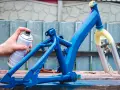 Ręka trzymająca puszkę z farbą w sprayu, malująca niebieską ramę roweru.