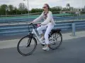 Kobieta w białych spodniach i sweterku jedzie na rowerze elektrycznym. Przepisy dotyczące rowerów elektrycznych są ważne dla bezpieczeństwa.