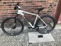 Biały rower Cube na tle ceglanej ściany. Wiele osób szuka rowery Cube opinie przed zakupem.