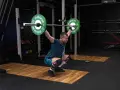 Mężczyzna w pozycji przysiadu z podniesionym sztangą, przygotowuje się do podrzutu. To element dwuboju olimpijskiego.