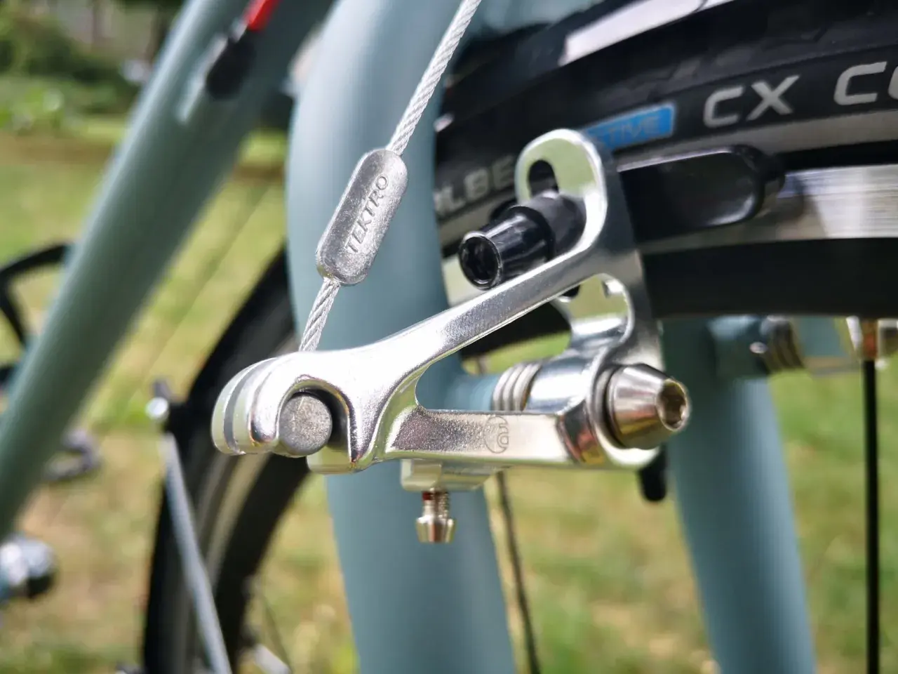 Szczegółowy widok hamulca szczękowego Tektro, jednego z rodzajów hamulców rowerowych, z widoczną linką i zaciskiem.