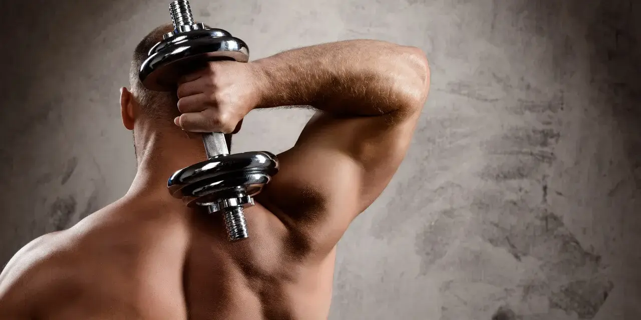Mężczyzna ćwiczy triceps z hantlem za głową, budując siłę i definicję mięśni.