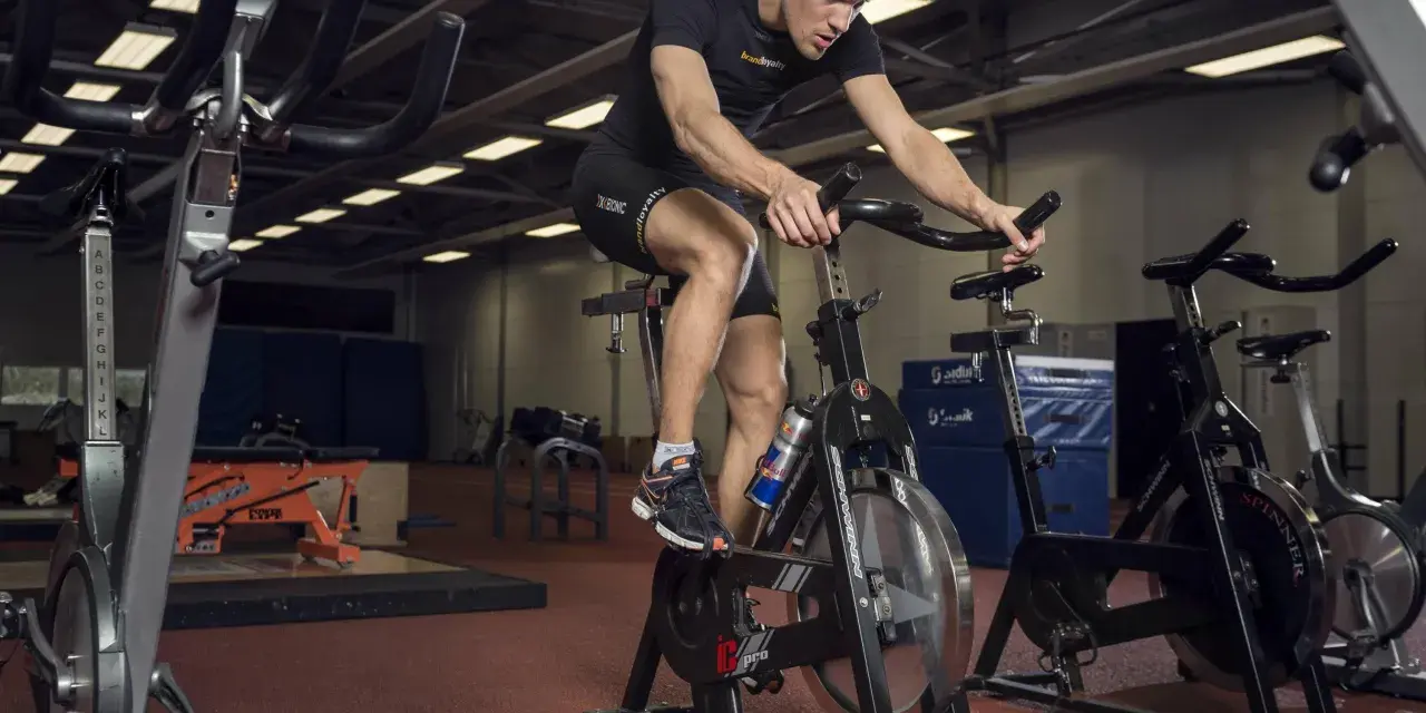 Mężczyzna intensywnie pedałuje na rowerze stacjonarnym, wykonując trening anaerobowy.