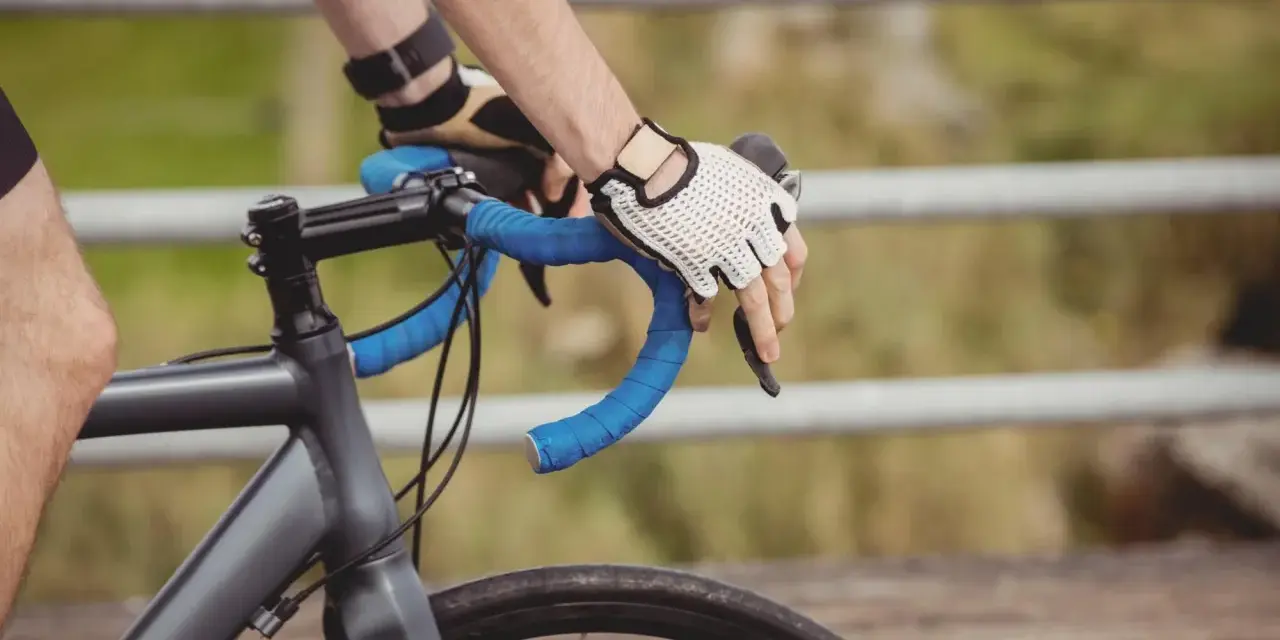 Rowerzysta w rękawiczkach trzyma kierownicę, zbliżając się do swojego progu mleczanowego.