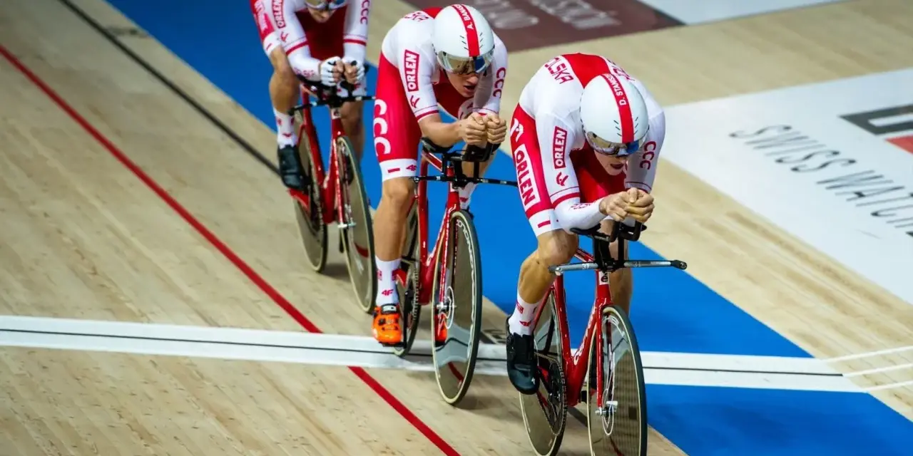 Trzech kolarzy w biało-czerwonych strojach ściga się na welodromie. Ich rowery i stroje mają logo ORLEN. To dynamiczne keirin kolarstwo.
