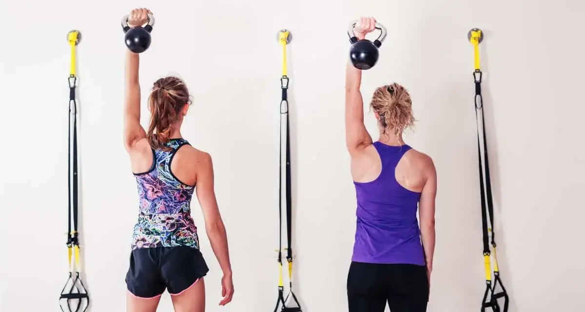 Dwie kobiety wykonują ćwiczenia z kettlebell, aby wzmocnić mięśnie i zapobiec bólowi barku.