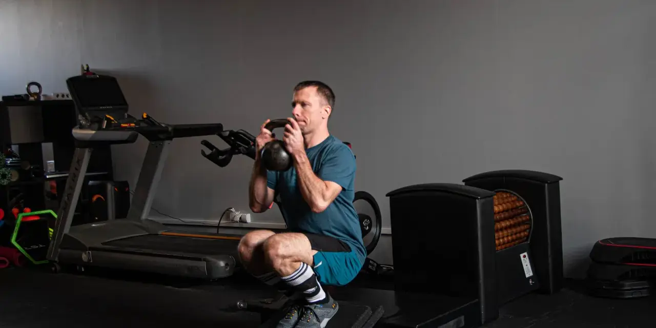 Mężczyzna wykonuje głęboki **squat** z kettlebell w rękach, ćwicząc siłę w siłowni.
