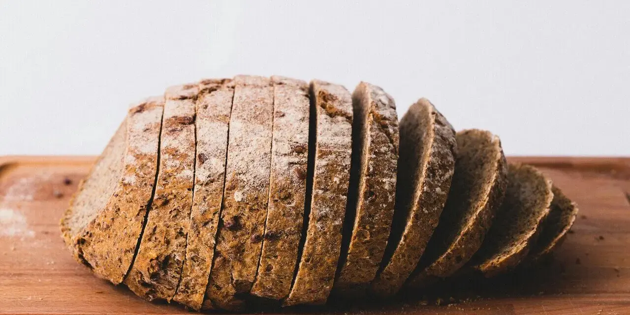 Pokrojony bochenek chleba żytniego na drewnianej desce. Zastanawiasz się, ile kcal ma kromka chleba?