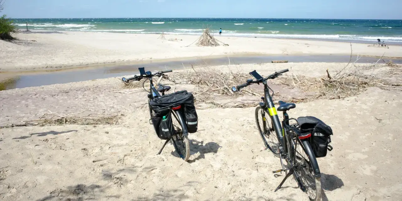 Dwa rowery z sakwami na piaszczystej plaży, gotowe do odkrywania tras rowerowych nad morzem.