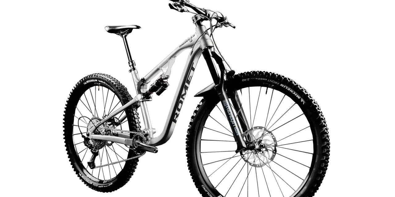 Srebrny rower MTB Romet Dagger 2.0 z pełnym zawieszeniem i oponami Michelin Wild Enduro. To sprzęt do pokonywania trudnych tras.