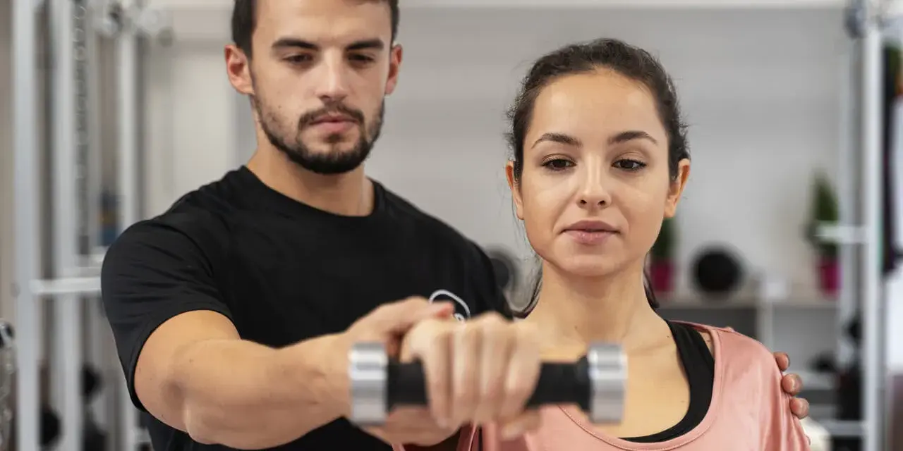 Trening dla początkujących: mężczyzna pomaga kobiecie podnosić hantle.