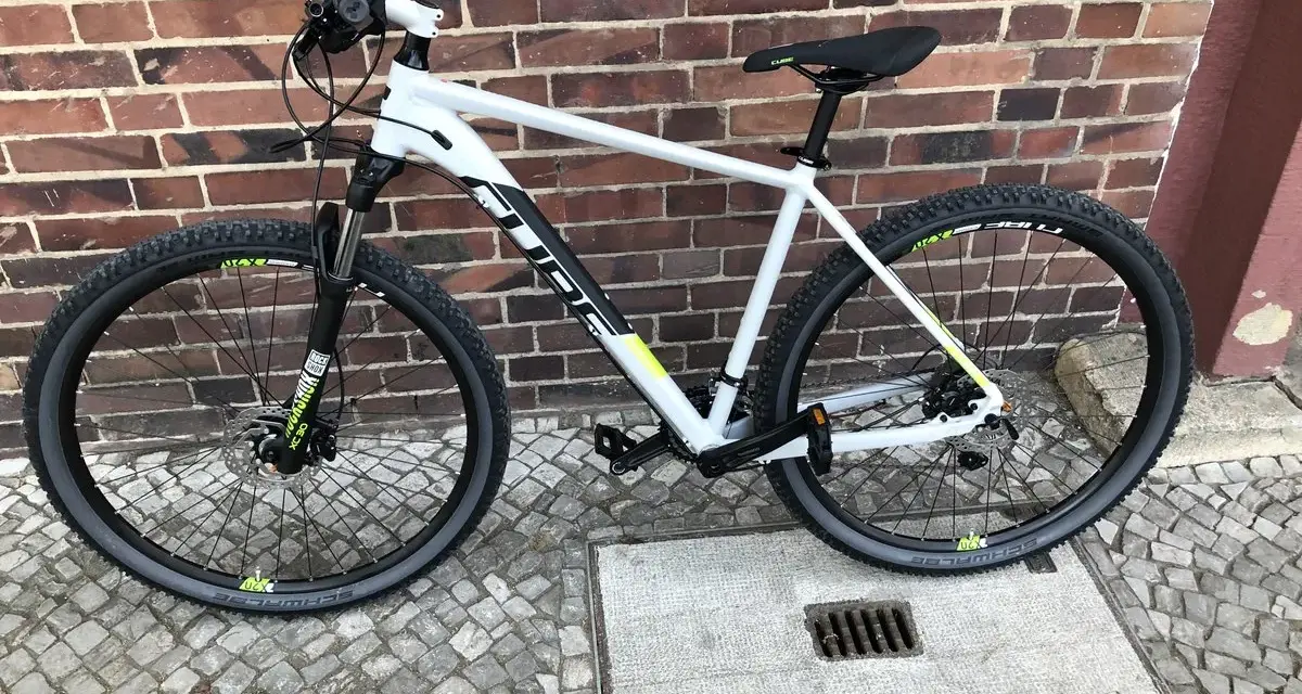 Biały rower Cube na tle ceglanej ściany. Wiele osób szuka rowery Cube opinie przed zakupem.