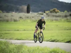 Kolarz w kasku i okularach na rowerze, pochylony do przodu, wykonuje intensywny trening beztlenowy na malowniczej drodze.
