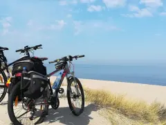 Dwa rowery z sakwami na plaży, gotowe na przygodę wzdłuż Velo Baltica. Morze i niebo tworzą tło.