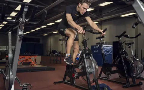 Mężczyzna intensywnie pedałuje na rowerze stacjonarnym, wykonując trening anaerobowy.