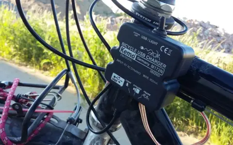 Ładowarka rowerowa Kemo zasilana przez **dynamo**, podłączona do kierownicy, z kablem USB.
