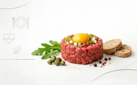 Tatar z surowego mięsa z żółtkiem i dodatkami, obok pieczywo. Czy tatar jest zdrowy? Zależy od składników i sposobu przygotowania.