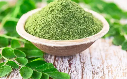 Zielony proszek z liści moringa w drewnianej miseczce, otoczony świeżymi liśćmi. Czy to ściema? Nie, to superfood!
