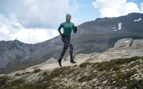 Kobieta w sportowym hidżabie biegnie po górskim szlaku, doskonaląc swoją kadencję w bieganiu.