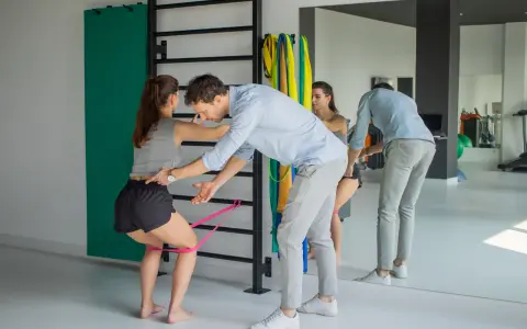 Fizjoterapeuta pomaga kobiecie w ćwiczeniach na kolana z użyciem taśmy oporowej.