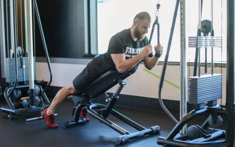 Mężczyzna wykonuje ćwiczenie na triceps, znane jako skull crushers, na ławce skośnej z użyciem wyciągu.