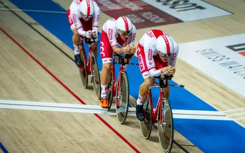 Trzech kolarzy w biało-czerwonych strojach ściga się na welodromie. Ich rowery i stroje mają logo ORLEN. To dynamiczne keirin kolarstwo.