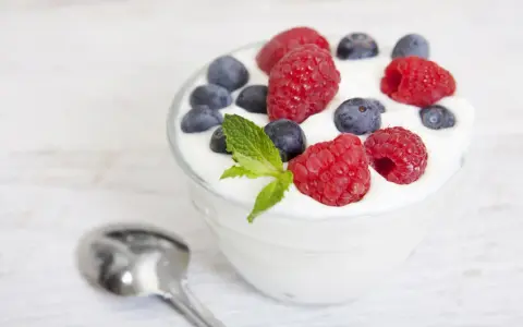 Pyszny jogurt z malinami i borówkami, idealny na śniadanie lub jako element diety jogurtowej. Obok leży łyżeczka.