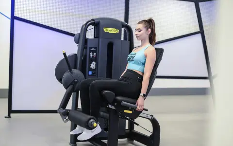Kobieta wykonuje wyprosty nóg na maszynie Technogym, ćwicząc mięśnie czworogłowe uda.