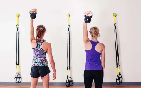 Dwie kobiety wykonują ćwiczenia z kettlebell, aby wzmocnić mięśnie i zapobiec bólowi barku.