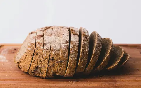 Pokrojony bochenek chleba żytniego na drewnianej desce. Zastanawiasz się, ile kcal ma kromka chleba?