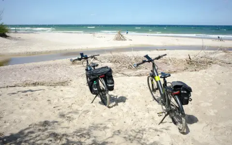 Dwa rowery z sakwami na piaszczystej plaży, gotowe do odkrywania tras rowerowych nad morzem.