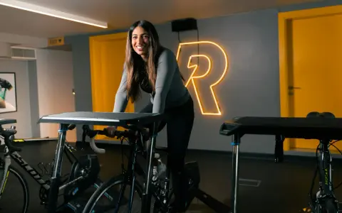 Uśmiechnięta kobieta na rowerze stacjonarnym, gotowa na intensywny trening cardio.