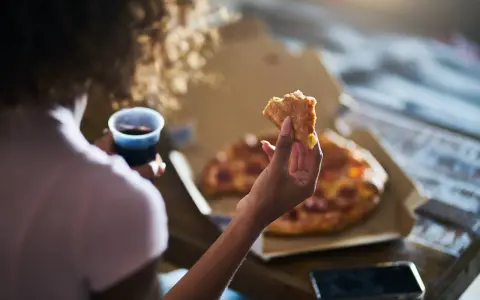 Kobieta trzyma kawałek pizzy i napój, czując głód. Grelina działa, apetyt rośnie.