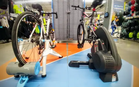 Dwa rowery na trenażerach, jeden z napędem direct drive, gotowe do treningu w sklepie sportowym.