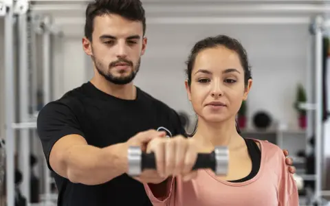 Trening dla początkujących: mężczyzna pomaga kobiecie podnosić hantle.